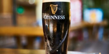 Close-up of a pint of Guinness stout beer on a wooden table in an indoor setting.