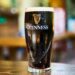 Close-up of a pint of Guinness stout beer on a wooden table in an indoor setting.