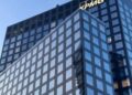 Glass facade of a modern office building in Milan with clear blue sky.